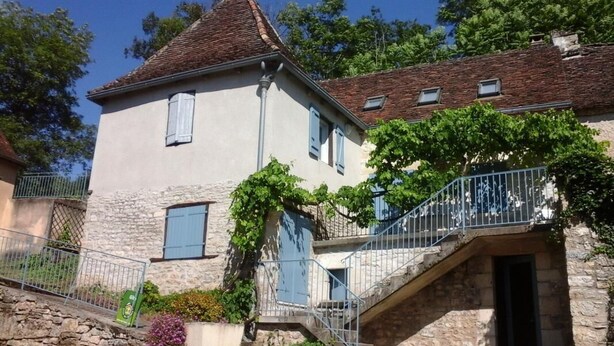 A stone building with a steep roof, a balcony with metal railings, and a staircase leading to the entrance. - Gîtes de France® - LA TOUR (CREYSSE)