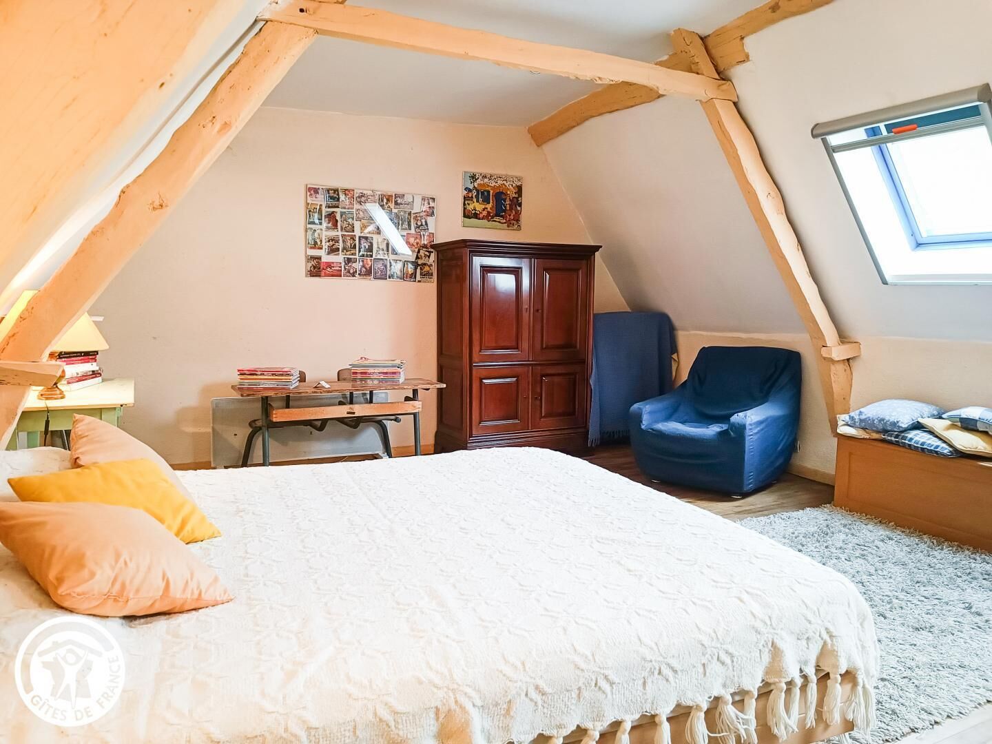 Een gezellige slaapkamer onder de dakpannen met een bed, een bureau met boeken, een kledingkast en een raam.