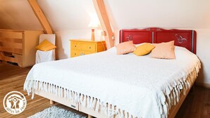 Ein Schlafzimmer mit geneigter Decke, einem Bett mit weißer Bettdecke, einem roten Kopfteil und einem gelben Nachttisch mit Lampe.
