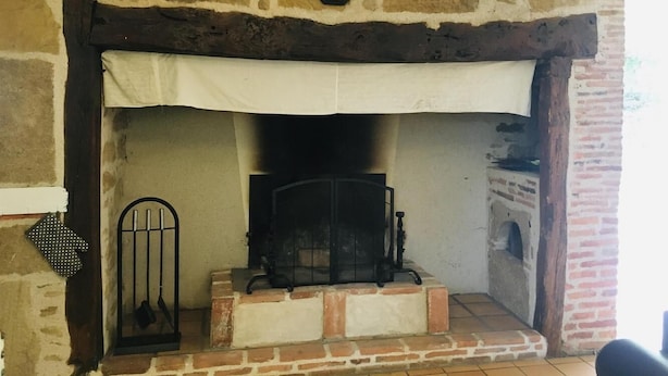 A stone fireplace with a white mantel, a clock above it, and a brick base. - Gîtes de France® - Les gites de La Grave 1 (CARDAILLAC)