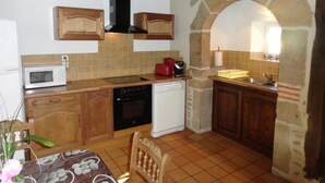 A kitchen with wooden cabinets, a microwave, a stove, and a dishwasher. - Gîtes de France® - Les gites de La Grave 1 (CARDAILLAC)