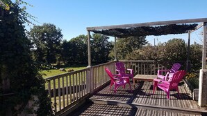 A wooden deck with a pergola, two pink Adirondack chairs, and a table. - Gîtes de France® - Les gites de La Grave 1 (CARDAILLAC)