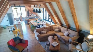An attic-style living space with a dining area, wooden beams, and a sofa. - Gîtes de France® - La Grange (FLAUJAC GARE)