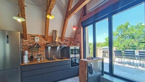 A modern kitchen with a brick wall, stainless steel appliances, and large windows overlooking a patio. - Gîtes de France® - La Grange (FLAUJAC GARE)