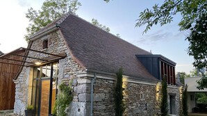 A stone house with a sloped roof, a wooden deck, and a stone pathway leading to the entrance. - Gîtes de France® - La Grange (FLAUJAC GARE)
