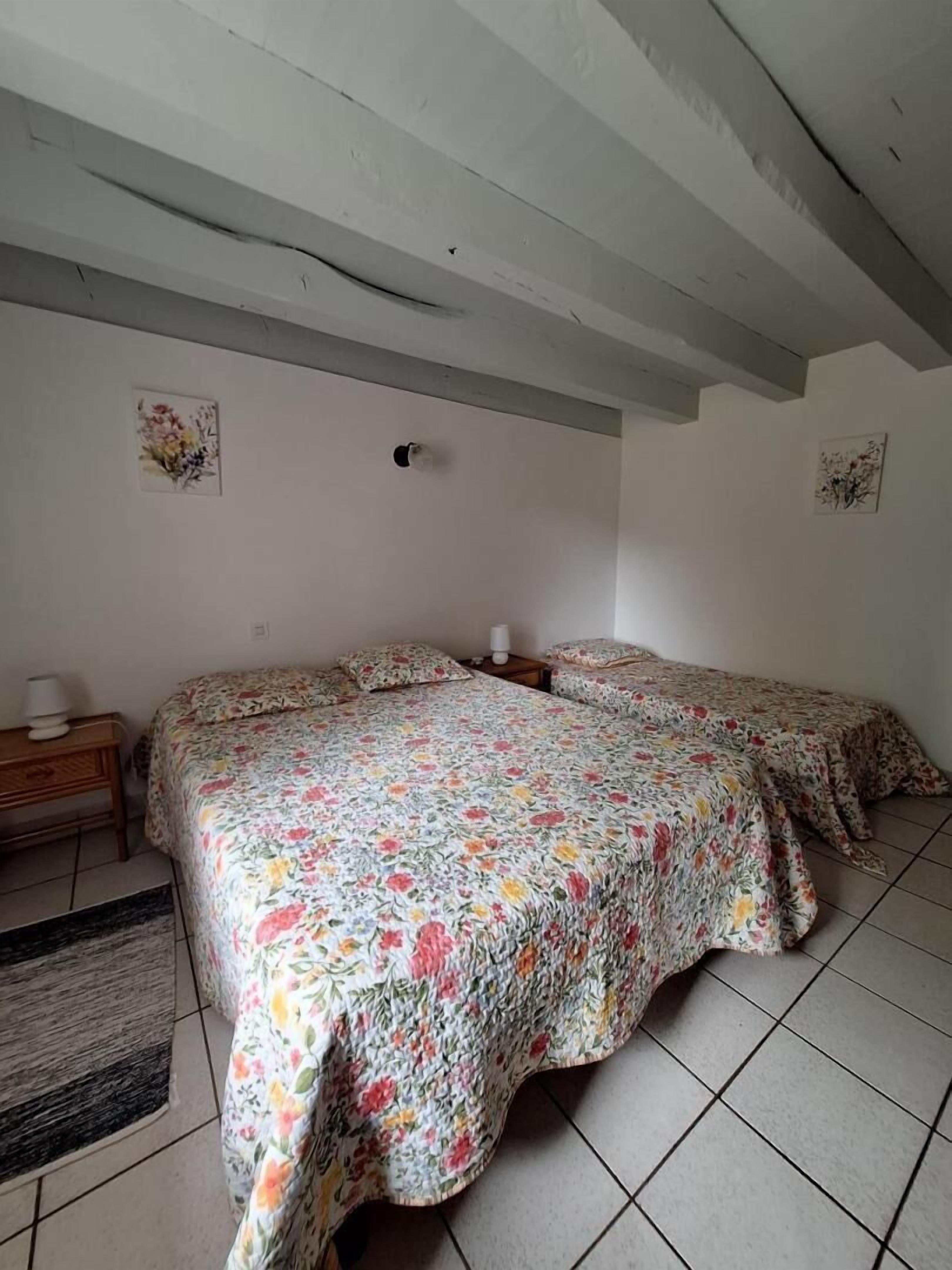 Quarto com duas camas, uma mesa pequena e luminária fixada na parede.