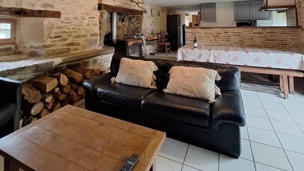 Un interior rústico con pared de piedra, vigas de madera, un sofá de cuero negro, una mesa de madera y una chimenea.