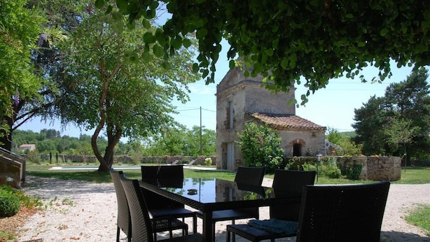 Ulkona sijaitseva ruokailualue, jossa on pöytä ja tuolit. Taustalla näkyy kivirakennus ja varjoa tuova puu.