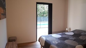 A bedroom with a bed, a small stool, a window, and a door. - Gîtes de France® - La Bouysse (SERIGNAC)