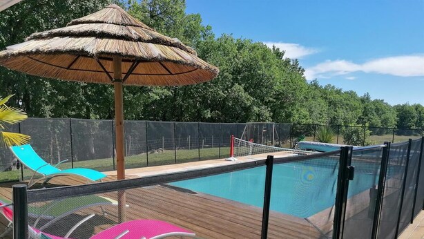 A pool with a wooden deck, a thatched umbrella, and colorful lounge chairs. - Gîtes de France® - La Bouysse (SERIGNAC)