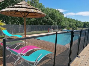 A pool with a wooden deck, a thatched umbrella, and colorful lounge chairs. - Gîtes de France® - La Bouysse (SERIGNAC)