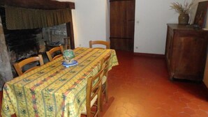 Un comedor con una mesa cubierta con un mantel estampado, sillas de madera, una chimenea y un aparador de madera con un jarrón y un marco de fotos.