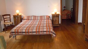 Un dormitorio con piso de madera, una cama con manta a rayas, dos mesitas de noche con lámparas y una silla.