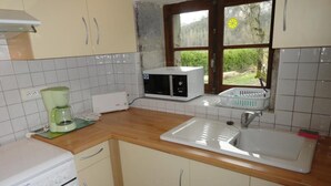 Una cocina con microondas, cafetera, pileta y armarios de madera.