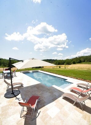 Ein rechteckiger Pool mit Fliesen umgeben, mit Liegestühlen und einem Tisch.