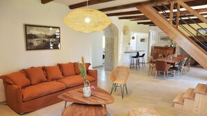 A spacious living area with a sofa, a round wooden coffee table, a wicker chair, and a staircase leading to another level. - Gîtes de France® - Gîte des Escures (SAINT CHELS)
