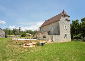 Ein Steinhaus mit Ziegeldach, einem kleinen Turm und einem Rasenstück mit Gartenmöbeln.
