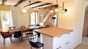 A modern kitchen with a large island, wooden dining table, and chairs. There is a staircase leading to an upper level. - Gîtes de France® - Gîte des Escures (SAINT CHELS)