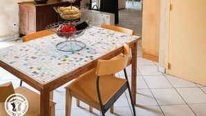 Un comedor con una mesa preparada para dos personas, una lámpara y vista a la cocina.