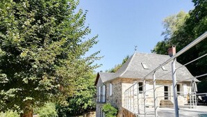 A stone house with a balcony overlooking a swimming pool, surrounded by trees and a clear sky. - Gîtes de France® - La Belle Lotoise (TEYSSIEU)