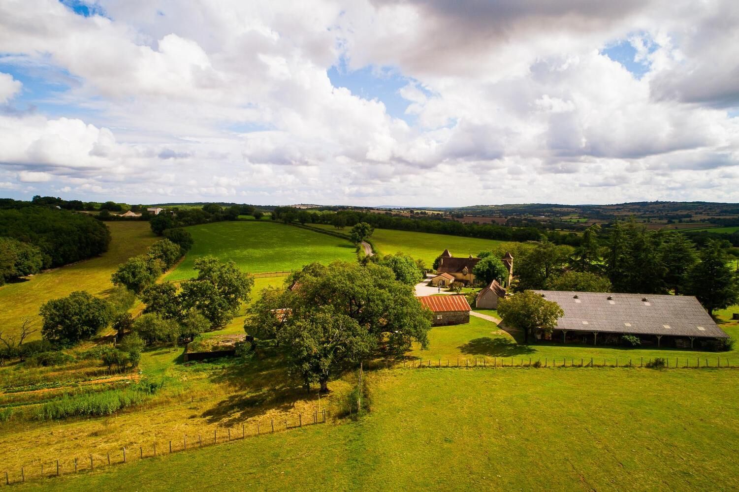 A rural landscape with a large barn, several trees, and rolling fields.