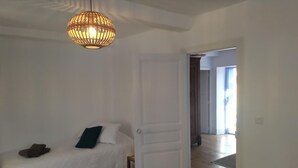 A bedroom with a bed, a white door, and a hallway leading to another room.