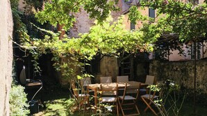 An outdoor dining area with a table and chairs, surrounded by greenery and a brick wall.