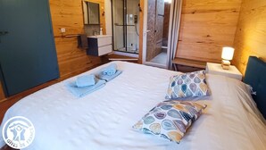 Ein Zimmer aus Holz mit einem Bett, einem Nachttisch, einem Spiegel, einem Badezimmer mit Dusche und einer Tür.