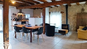 Ein rustikales Interieur mit freiliegenden Holzbalken, einer Steinwand, einem Kamin und einer Essecke mit Tisch und Stühlen.