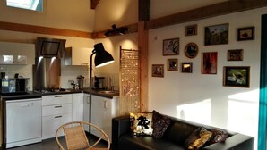Uma sala de estar aconchegante com um sofá de couro preto, uma poltrona de vime e um espaço de jantar com fogão e micro-ondas.
