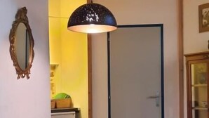 Uma área de refeições com uma mesa de madeira e cadeiras pretas, uma luminária pendente e uma porta ao fundo.