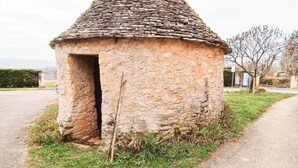 Ein kleines Steinhaus mit einem Strohdach, gelegen auf einer grünen Wiese neben einer asphaltierten Straße.