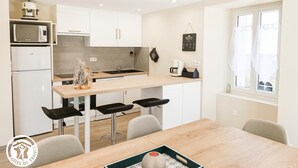 A modern kitchen with white cabinets, a wooden island, and a dining area with a table and chairs. - Gîtes de France® - Gîte du Fau (BESSONIES)