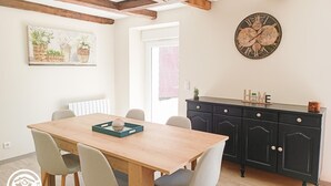 A dining area with a wooden table and chairs, a black cabinet with drawers, and a wall clock. - Gîtes de France® - Gîte du Fau (BESSONIES)