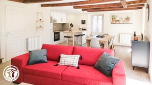 A modern apartment with a red sofa, kitchen, dining area, and exposed wooden beams. - Gîtes de France® - Gîte du Fau (BESSONIES)