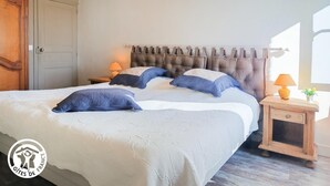 A bedroom with a large bed, a wooden wardrobe, a nightstand with a lamp, and a window with curtains.