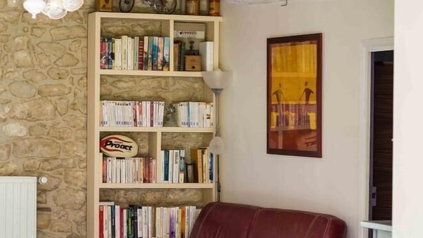 Una sala de estar acogedora con un sofá de cuero rojo, una estantería llena de libros y una pared de piedra.