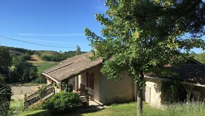 A rustic stone house with a thatched roof, a wooden porch, and a small garden area.