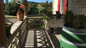 A covered outdoor area with a wooden railing, potted plants, and a view of a rural landscape.