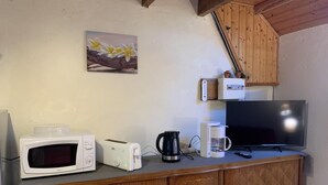 Une petite cuisine équipée d’un four à micro-ondes, d’un grille-pain, d’une machine à café et d’un téléviseur posé sur un meuble en bois.
