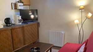 Une pièce chaleureuse avec un canapé rouge, des meubles en bois, une télévision, une machine à café et une lucarne.