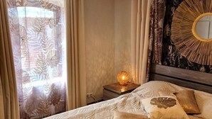 Un letto rifatto con una coperta a motivi, una lampada da comodino e un muro con uno specchio decorativo.