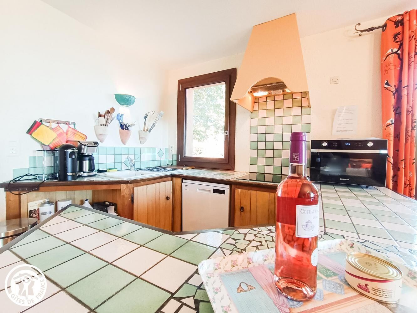 Une cuisine avec des meubles de rangement en bois, une machine à café, une bouteille de vin et un four à micro-ondes.
