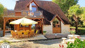 A rustic building with a stone and wooden facade, a covered patio with a table and chairs, and a small garden area.