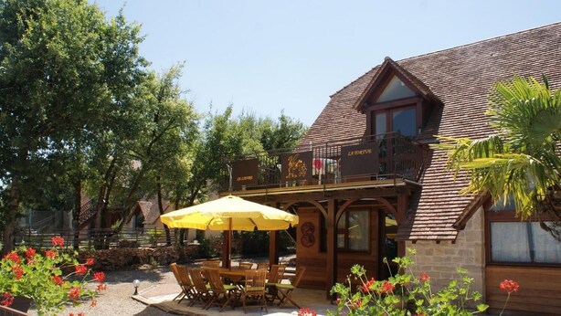 A wooden building with a balcony, outdoor seating, and a yellow umbrella.