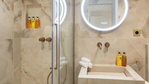 A modern bathroom with a glass-enclosed shower, a vanity with a mirror, and toiletries.