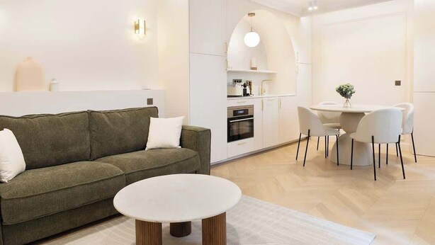 A modern living room with a green sofa, a white coffee table, and a dining area with a white table and chairs.