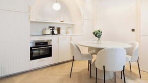 A modern kitchen with white cabinetry, a built-in oven, and a round dining table with chairs.