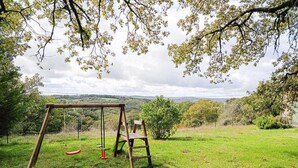 A swing set in a grassy field with a view of distant hills.