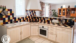 A kitchen with a colorful tile backsplash, wooden cabinets, a window with curtains, and a hanging light fixture.